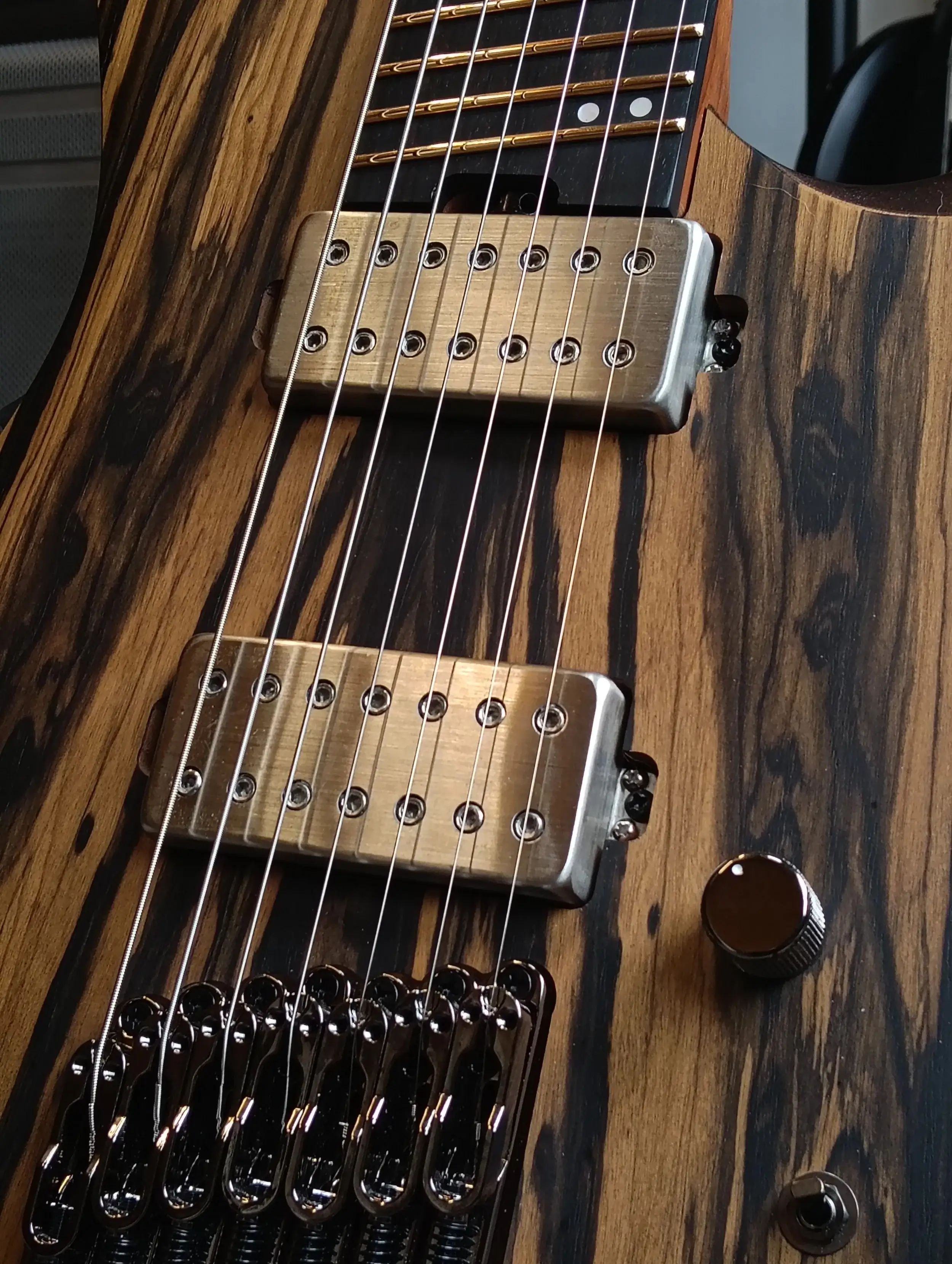 Close-up van twee open-coil humbuckers en de brugzadels op een gitaar met een donker gestreepte ziricote-top.